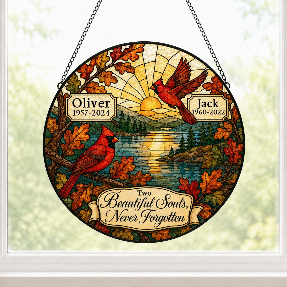 Two red cardinals with a glowing sun over a mountain lake and pine trees, framed by autumn oak leaves on a round suncatc