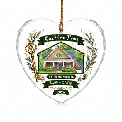 Heart-shaped glass ornament with watercolor house, gold key, evergreens, green banners, and 'Our New Home' text.