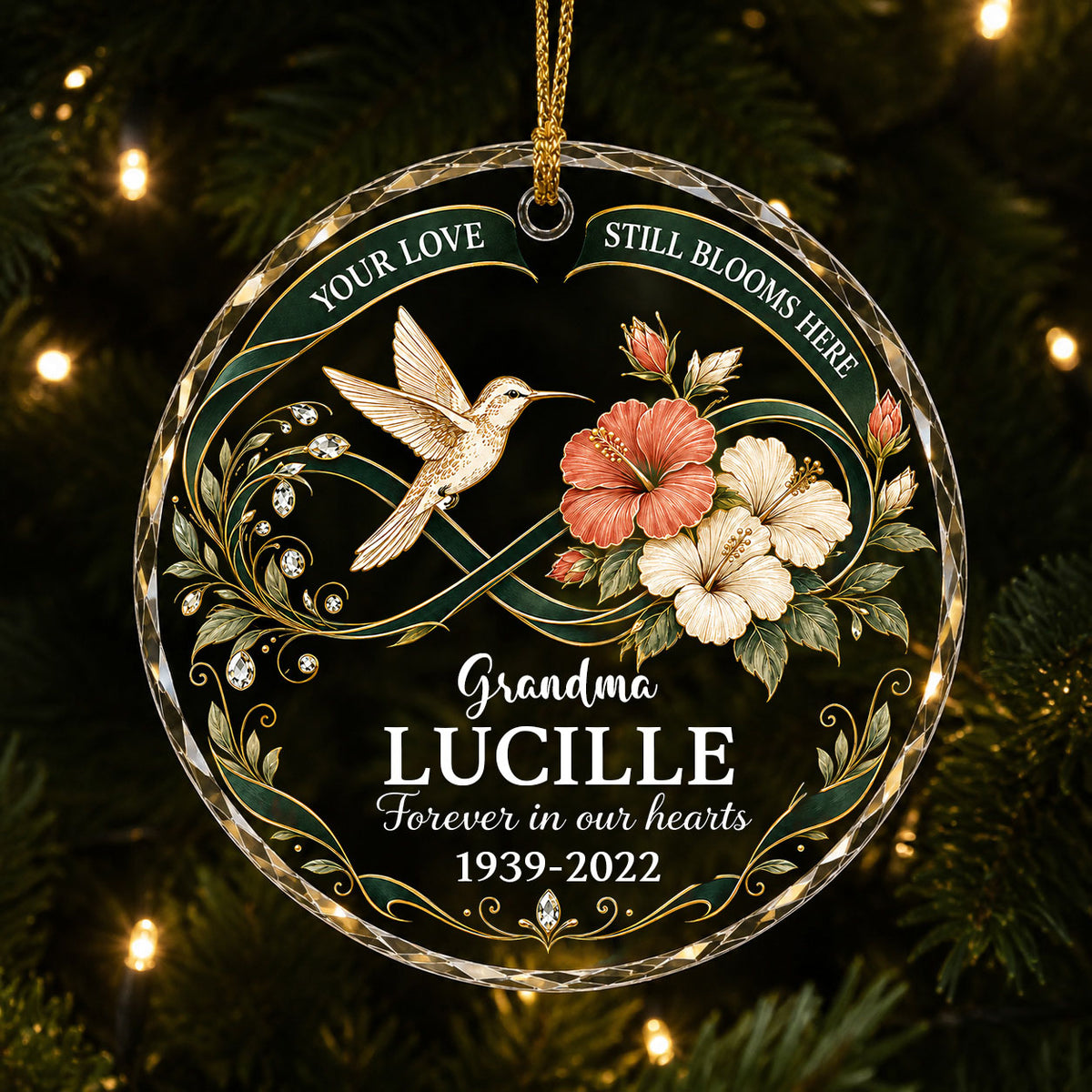 Round glass ornament with hummingbird, hibiscus, green infinity ribbon, and 'Your Love Still Blooms Here' text.