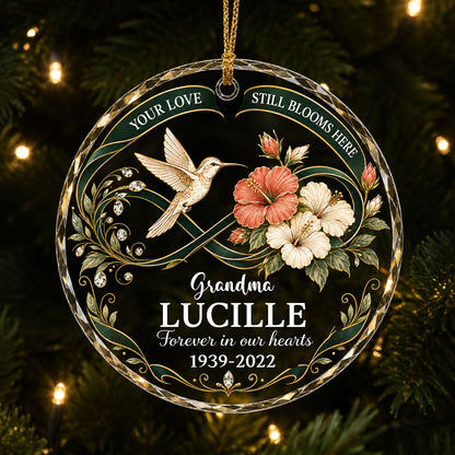 Round glass ornament with hummingbird, hibiscus, green infinity ribbon, and 'Your Love Still Blooms Here' text.