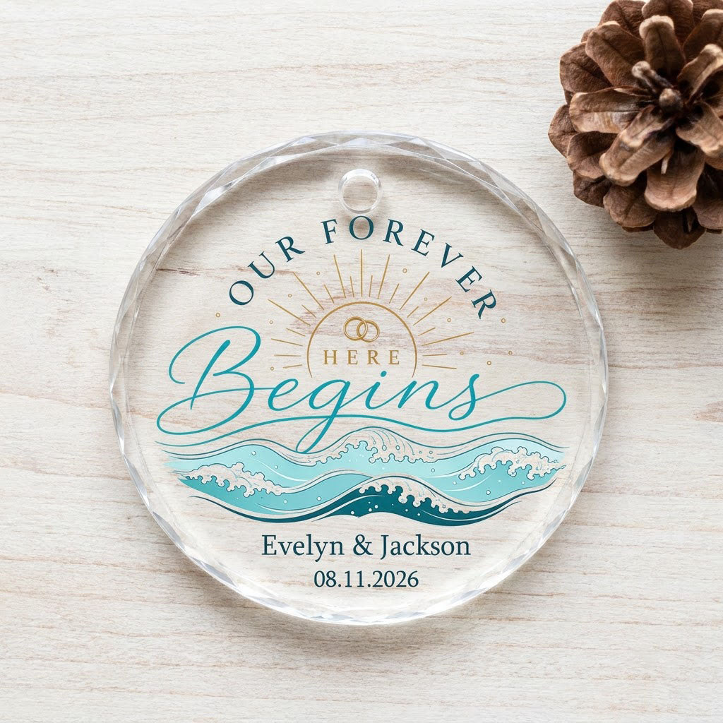 Round glass ornament with gold sun, interlocking rings, teal ocean waves, and 'OUR FOREVER HERE Begins' text.