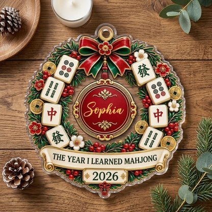 A clear acrylic wreath ornament with Mahjong tiles, red bow, gold coins, and the text THE YEAR I LEARNED MAHJONG.