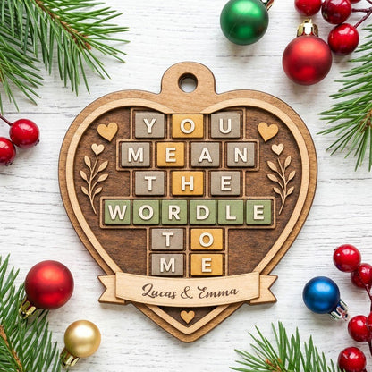 Heart-shaped wood ornament with Wordle-style tiles reading You Mean The Wordle To Me and names on a bottom banner.