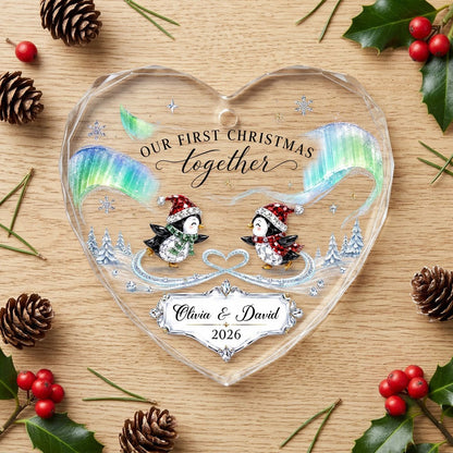Heart glass ornament with two ice-skating penguins under green and blue aurora with names and date.