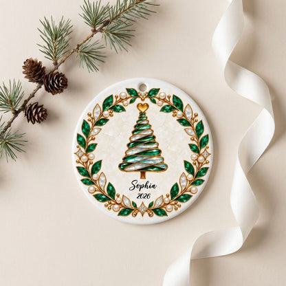 Round ceramic ornament with an emerald jeweled spiral Christmas tree and gold filigree wreath on cream.