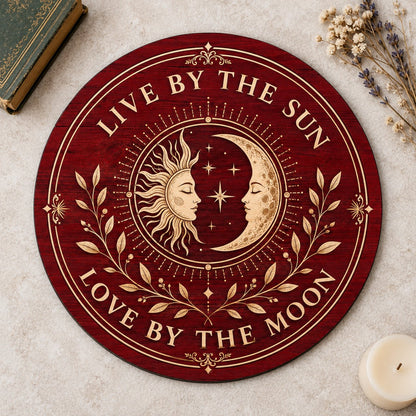 Round wooden sign with sun and crescent moon faces, stars, vines, and the quote Live by the Sun, Love by the Moon.