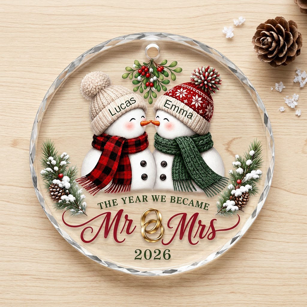 Round faceted glass ornament with two kissing snowmen under mistletoe and gold rings, personalized with names.