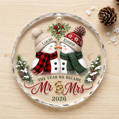 Round faceted glass ornament with two kissing snowmen under mistletoe and gold rings, personalized with names.