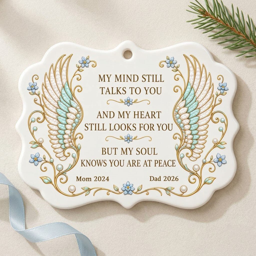 Medallion ceramic ornament with gold-outlined angel wings, blue forget-me-nots, and a memorial quote with name and year.