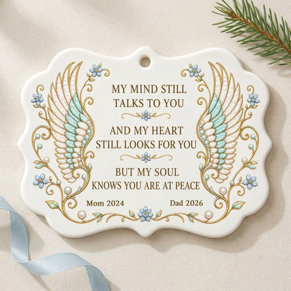Medallion ceramic ornament with gold-outlined angel wings, blue forget-me-nots, and a memorial quote with name and year.