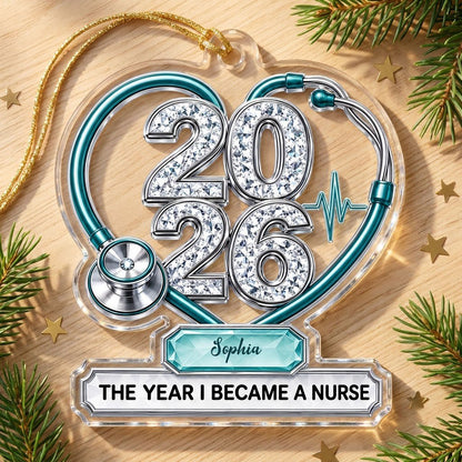 Clear acrylic ornament with a teal stethoscope heart, diamond 2026 numerals, teal ECG wave, and a personalized name bann