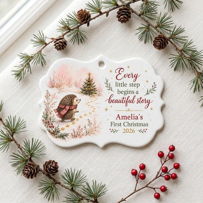 Scalloped ceramic ornament with hedgehog in red plaid scarf walking toward a decorated Christmas tree in the snow.