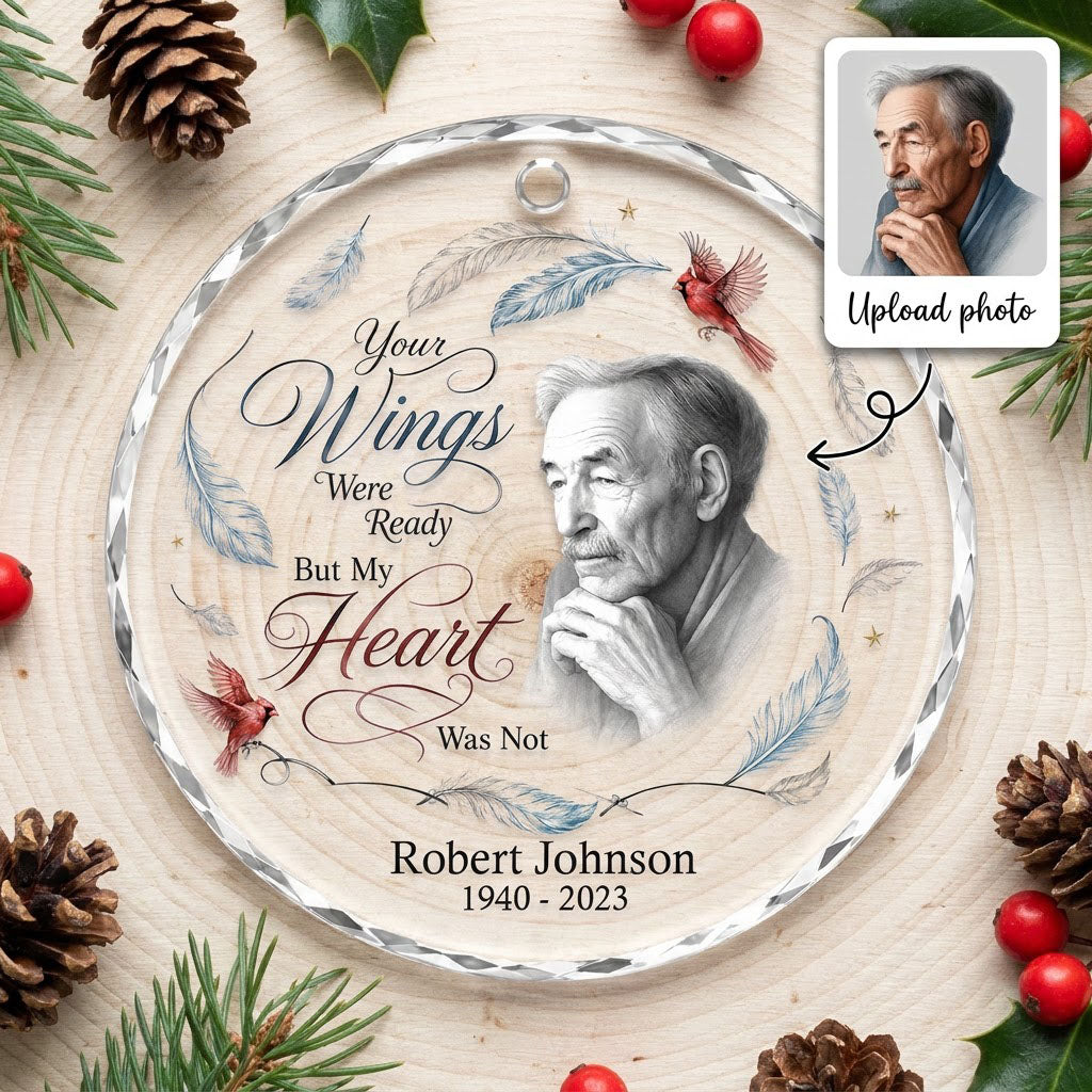 Round glass ornament with sketch portrait, two red cardinals, blue and brown feathers, and memorial name and years.