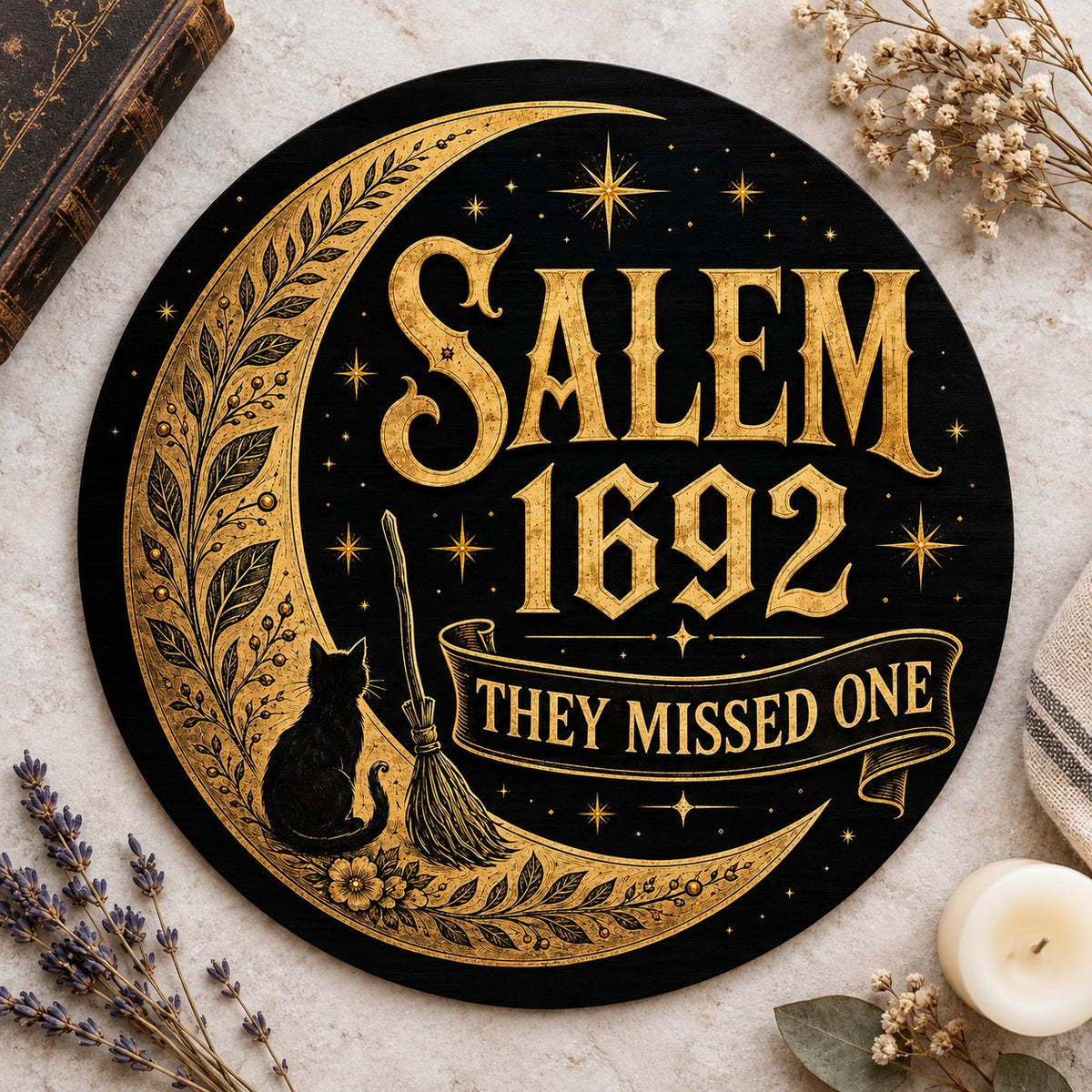 Round wooden sign with gold crescent moon, black cat, broomstick, stars and 'SALEM 1692 THEY MISSED ONE' on black.