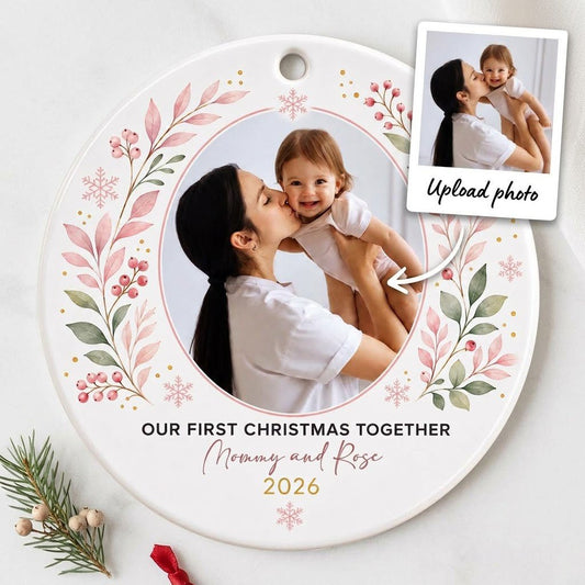 Round ceramic ornament with a photo frame, pink-green botanical wreath, and 'OUR FIRST CHRISTMAS TOGETHER' text.