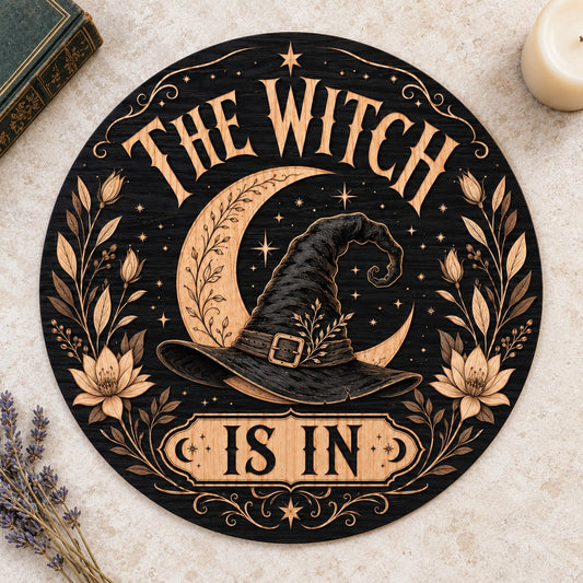 Round wooden sign with 'THE WITCH IS IN' slogan, crescent moon, witch hat, floral borders, stars and scrollwork.