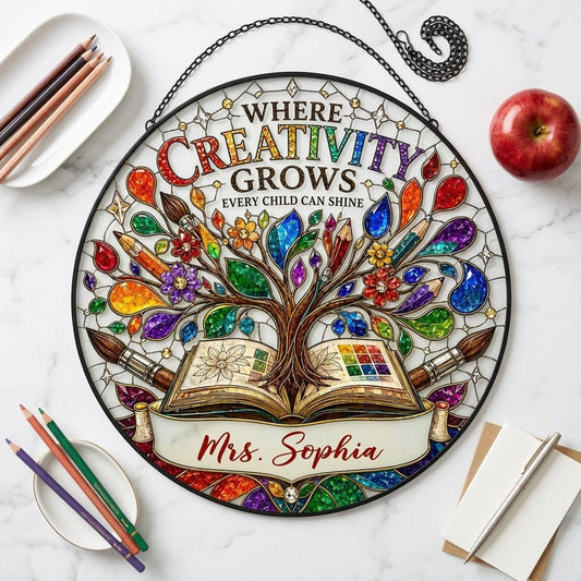 Round stained glass-style suncatcher with tree growing from an open book, paintbrushes, pencils, blossoms, and teacher n