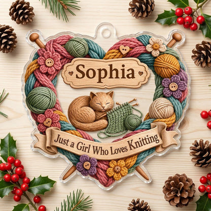 Heart-shaped acrylic ornament with yarn wreath, knitting needles, brown cat and "Just a Girl Who Loves Knitting" text.