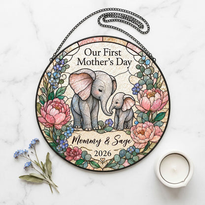 Round stained-glass suncatcher of mother and baby elephants touching trunks amid pink peonies and blue flowers.