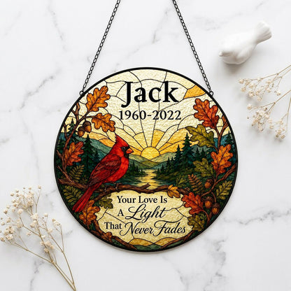 Round stained-glass style suncatcher with a red cardinal, oak leaves, mountains, a river and a radiant sun.