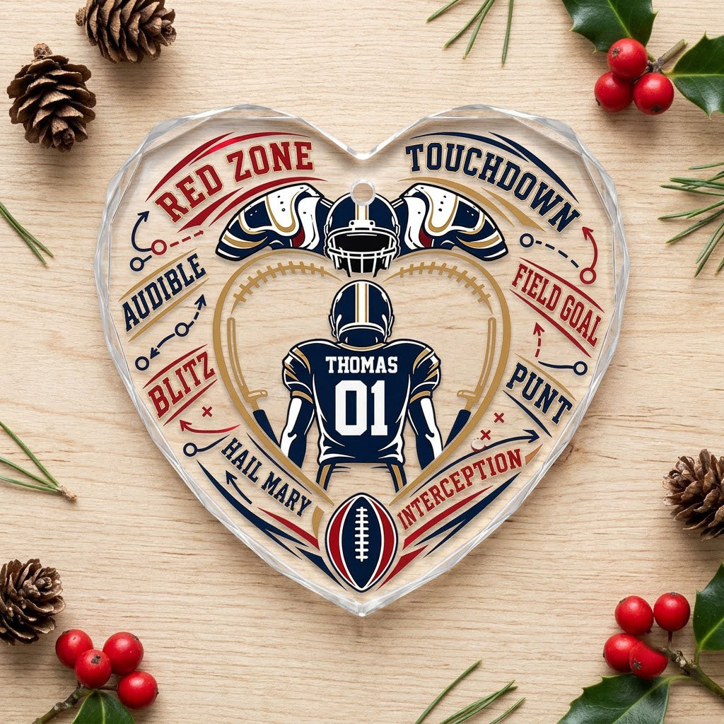 Heart-shaped glass ornament with back-view football player, gold stitched heart frame, football, and play diagram elemen