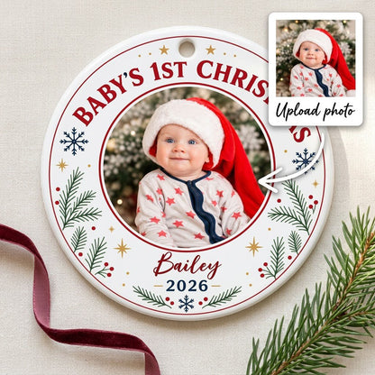 Round ceramic ornament with 'BABY'S 1ST CHRISTMAS', pine sprigs, snowflakes, gold stars, red rings, and a photo frame