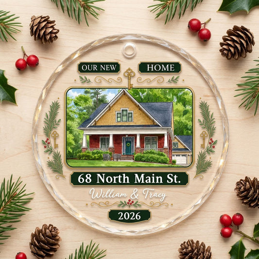 Round glass ornament with watercolor house, green and gold banners, gold key, pine branches, and address and year plaque