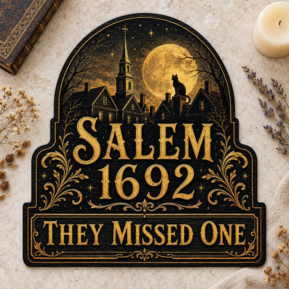 Custom-cut wooden sign reading “SALEM 1692” and “THEY MISSED ONE” with a black cat on a moonlit village and gold filigre