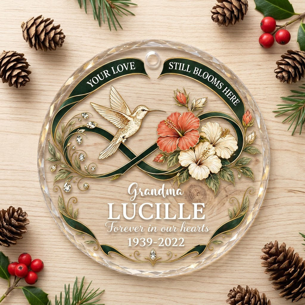 Round glass ornament with hummingbird, hibiscus, green infinity ribbon, and 'Your Love Still Blooms Here' text.