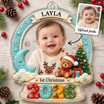 Acrylic snow-globe ornament with baby photo, "1st Christmas", teddy bear, moon, clouds, and big 2026 at the base.
