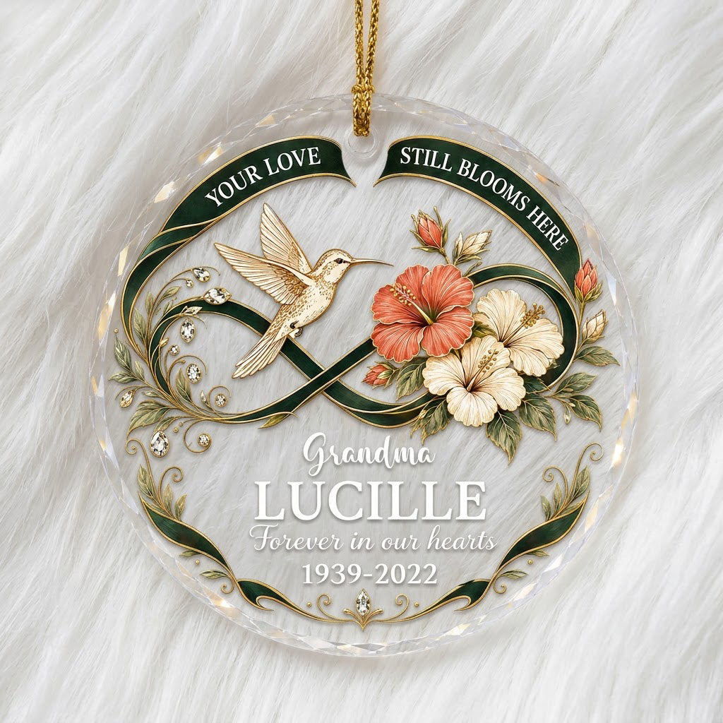Round glass ornament with hummingbird, hibiscus, green infinity ribbon, and 'Your Love Still Blooms Here' text.