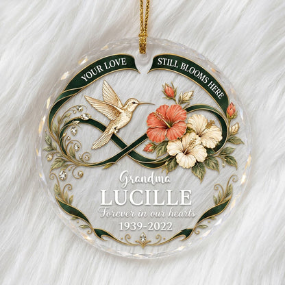 Round glass ornament with hummingbird, hibiscus, green infinity ribbon, and 'Your Love Still Blooms Here' text.