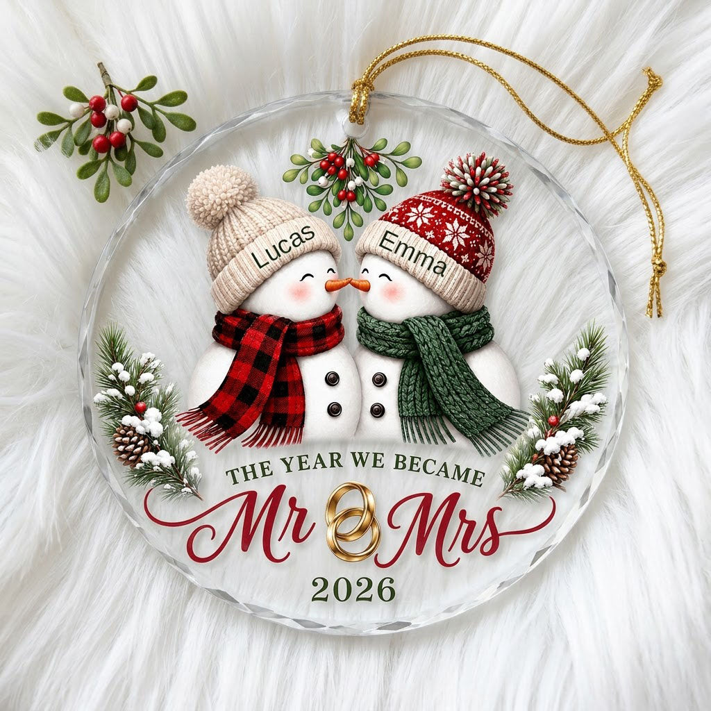 Round faceted glass ornament with two kissing snowmen under mistletoe and gold rings, personalized with names.