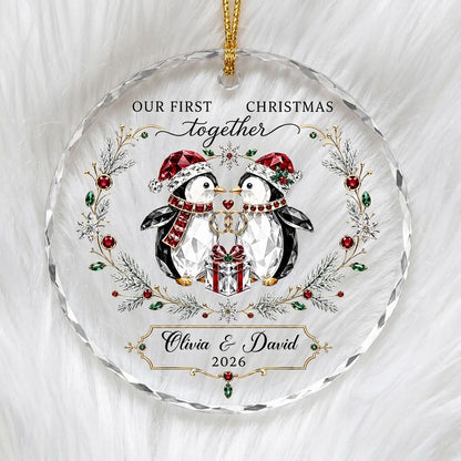 Penguin couple in Santa hats hold gold rings beneath a heart, framed by a pine and gem wreath with a gift box.