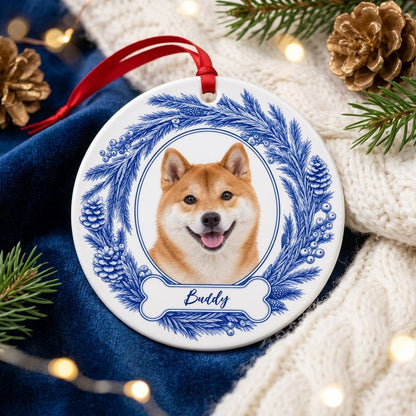 Round ceramic ornament with blue pine wreath, oval dog photo frame, and a blue-outlined bone at the bottom.