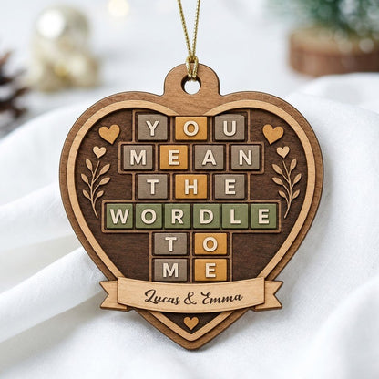 Heart-shaped wood ornament with Wordle-style tiles reading You Mean The Wordle To Me and names on a bottom banner.