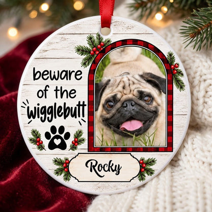 Round ceramic ornament with buffalo plaid photo frame, paw-heart, pine sprigs, and 'beware of the Wigglebutt'.