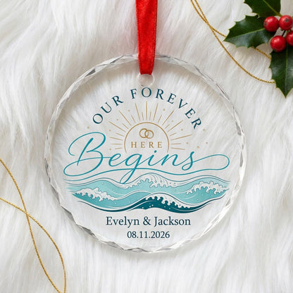 Round glass ornament with gold sun, interlocking rings, teal ocean waves, and 'OUR FOREVER HERE Begins' text.