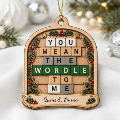 Arch wood ornament with “You Mean The Wordle To Me” letter tiles, evergreen sprigs with red berries, gold stars, and cou