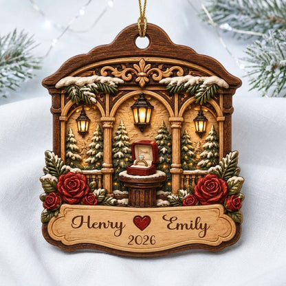Arched wood ornament with three lanterns, pine trees, red roses, and an open ring box on a central pedestal.