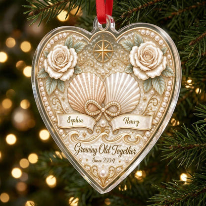 Heart-shaped clear acrylic ornament with seashells, pearl infinity symbol, compass star, and two name ribbons.