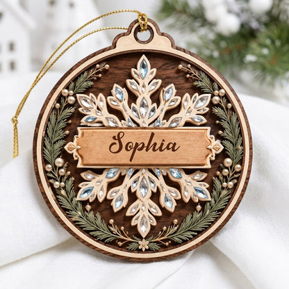 Round wood ornament with a snowflake, gemstone accents, pine sprigs, and a banner personalized with a name.