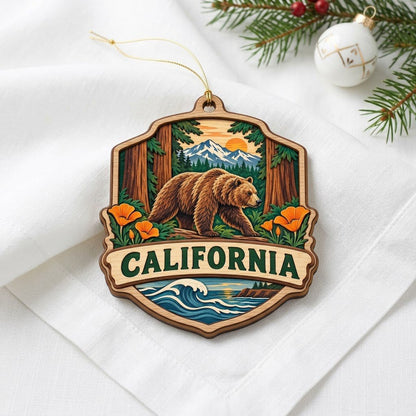 Shield-shaped wood ornament reading CALIFORNIA with bear on log, poppies, redwoods, mountains, and ocean waves.