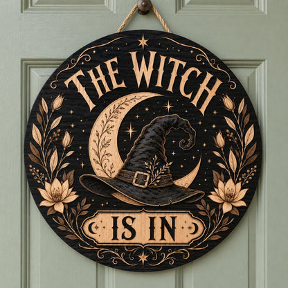 Round wooden sign with 'THE WITCH IS IN' slogan, crescent moon, witch hat, floral borders, stars and scrollwork.