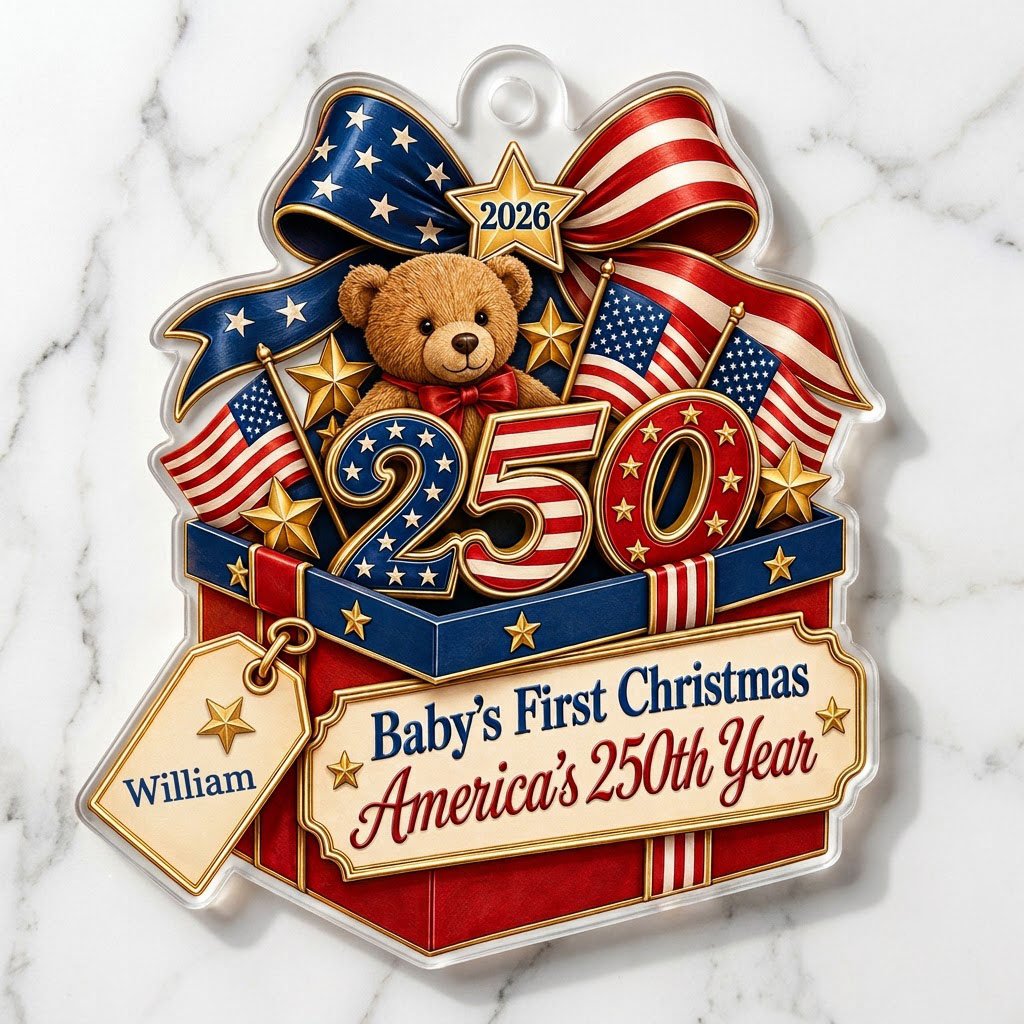A teddy bear in a red gift box with blue trim, 250 and 2026 with American flags and a patriotic bow on an acrylic orname