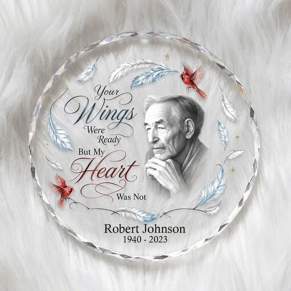Round glass ornament with sketch portrait, two red cardinals, blue and brown feathers, and memorial name and years.
