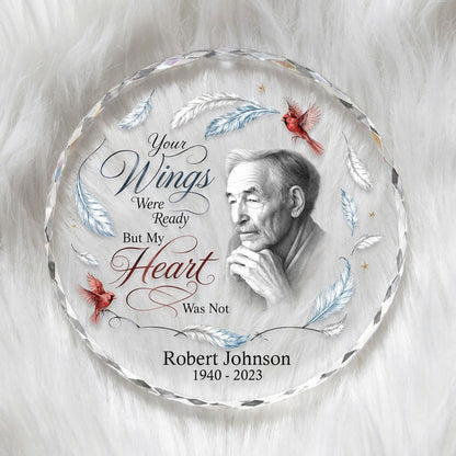 Round glass ornament with sketch portrait, two red cardinals, blue and brown feathers, and memorial name and years.
