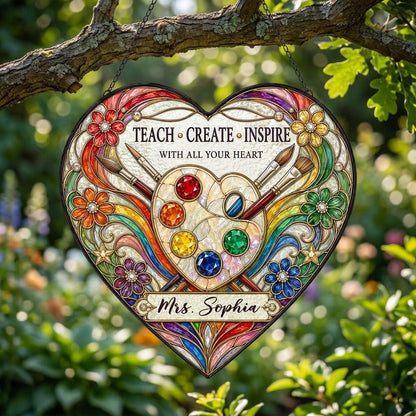 Heart-shaped stained glass suncatcher with palette, brushes, rainbow arcs, flowers and 'Teach • Create • Inspire'.
