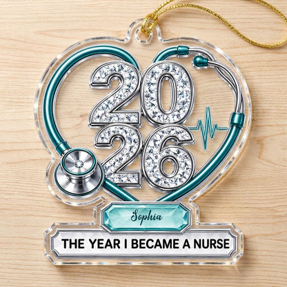 Clear acrylic ornament with a teal stethoscope heart, diamond 2026 numerals, teal ECG wave, and a personalized name bann