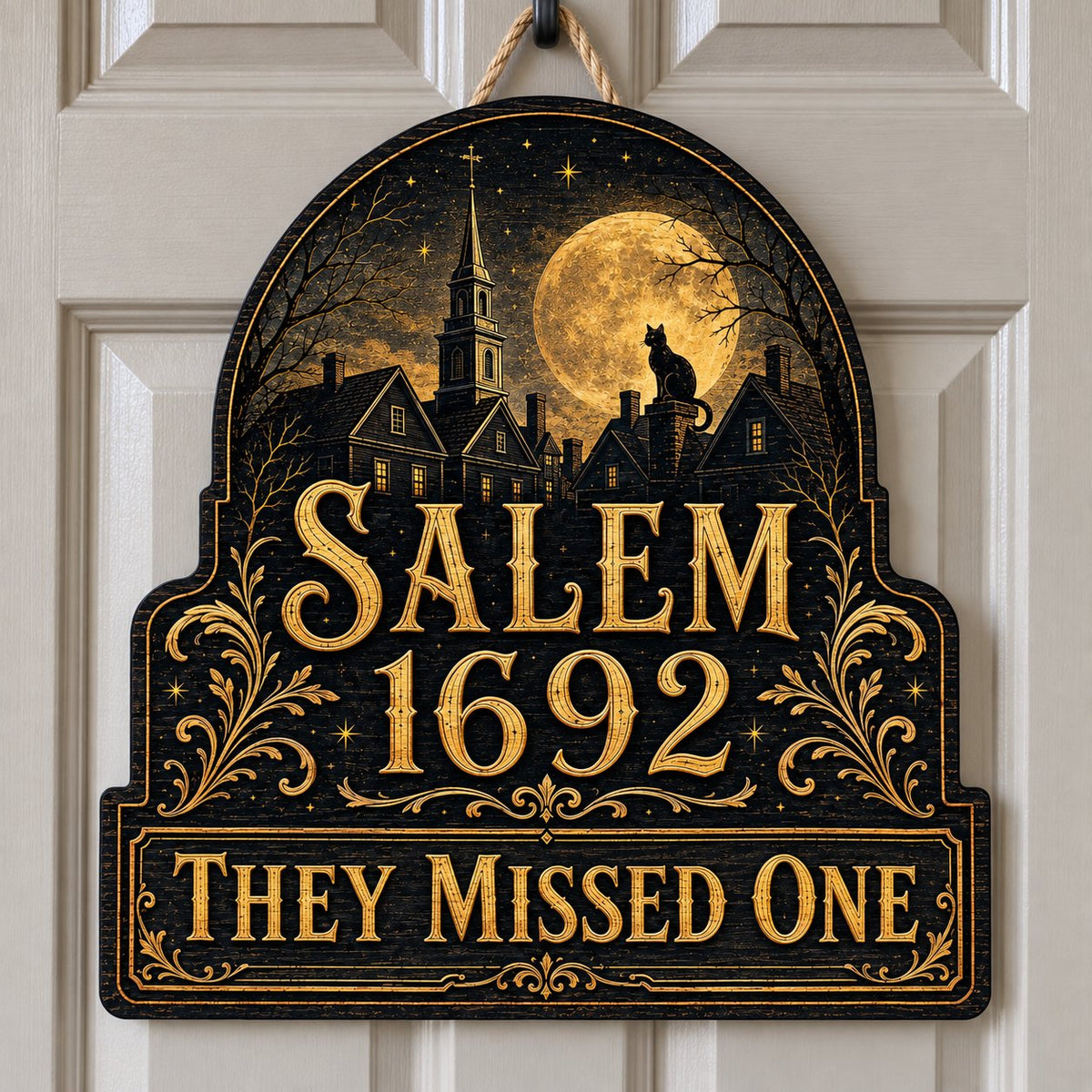 Custom-cut wooden sign reading “SALEM 1692” and “THEY MISSED ONE” with a black cat on a moonlit village and gold filigre